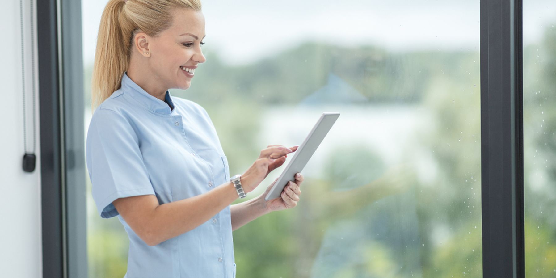 A nurse reviewing patient notes on a tablet by a window